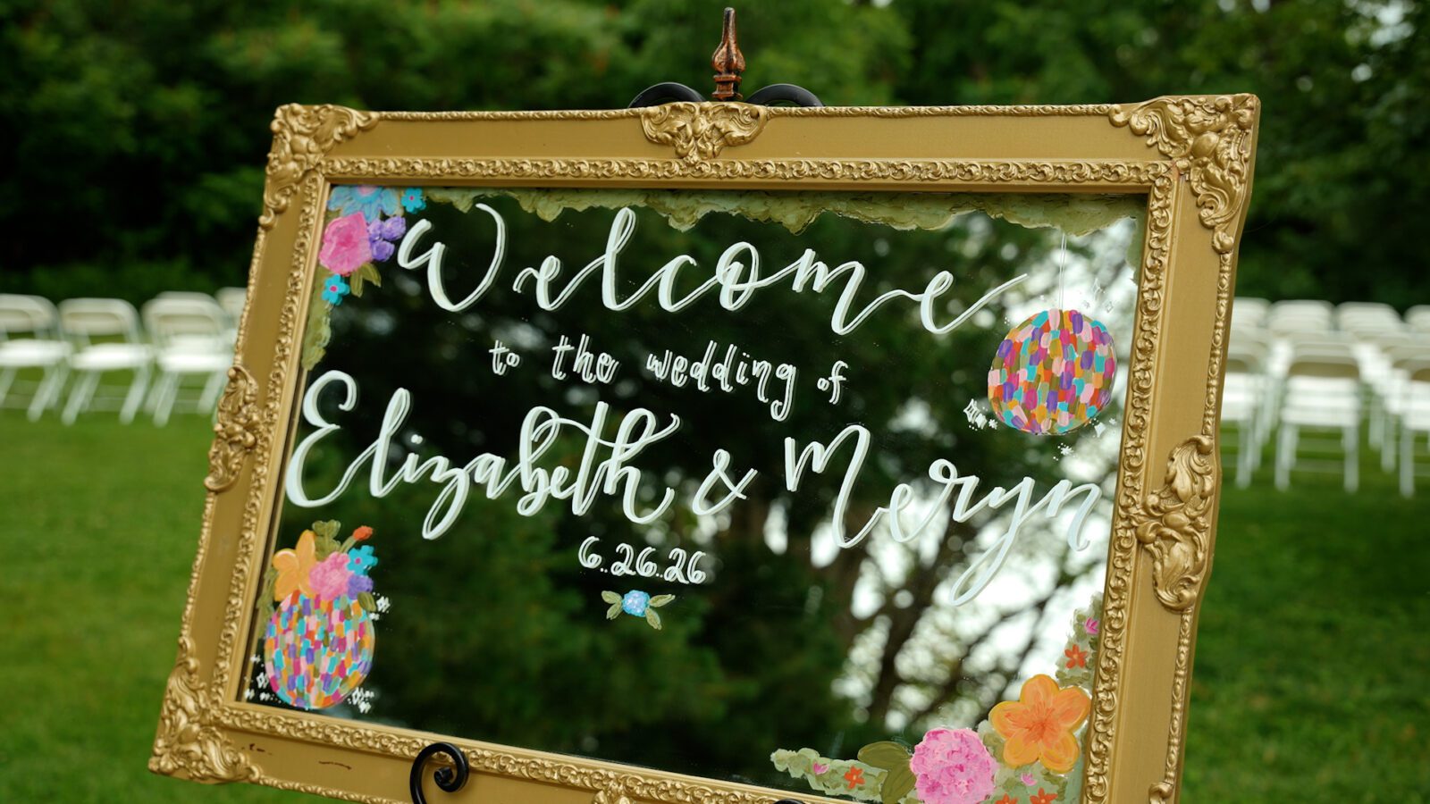 Gold framed mirror welcome sign decorated with colorful painted flowers and disco balls at District 5 Schoolhouse.