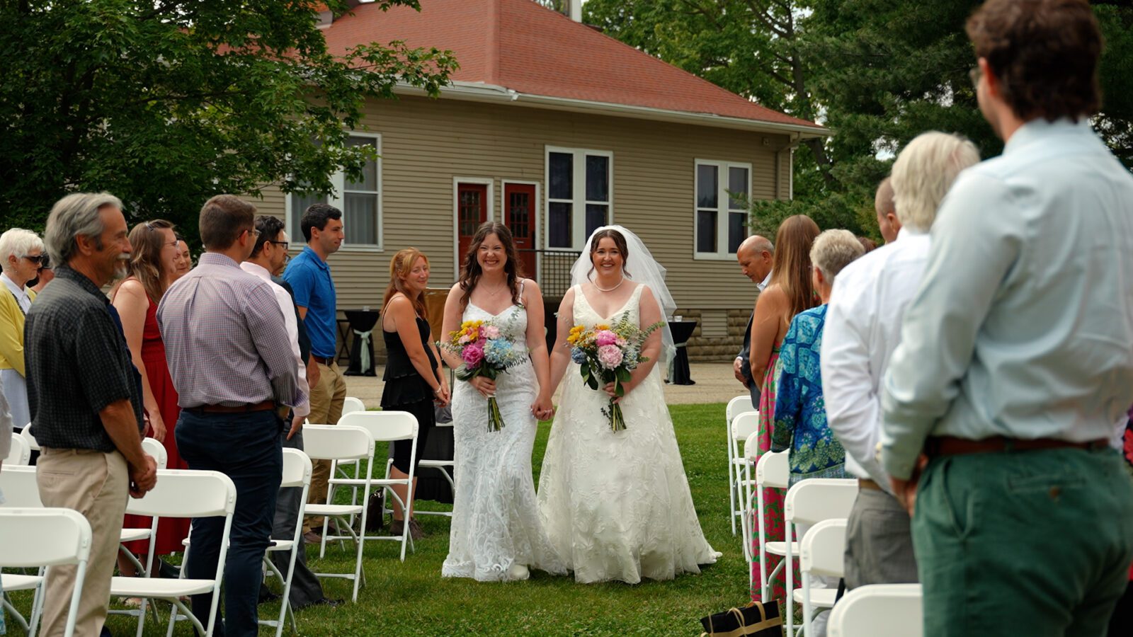 Newlyweds smiling and walking down the aisle together while holding colorful wildflower bouquets.