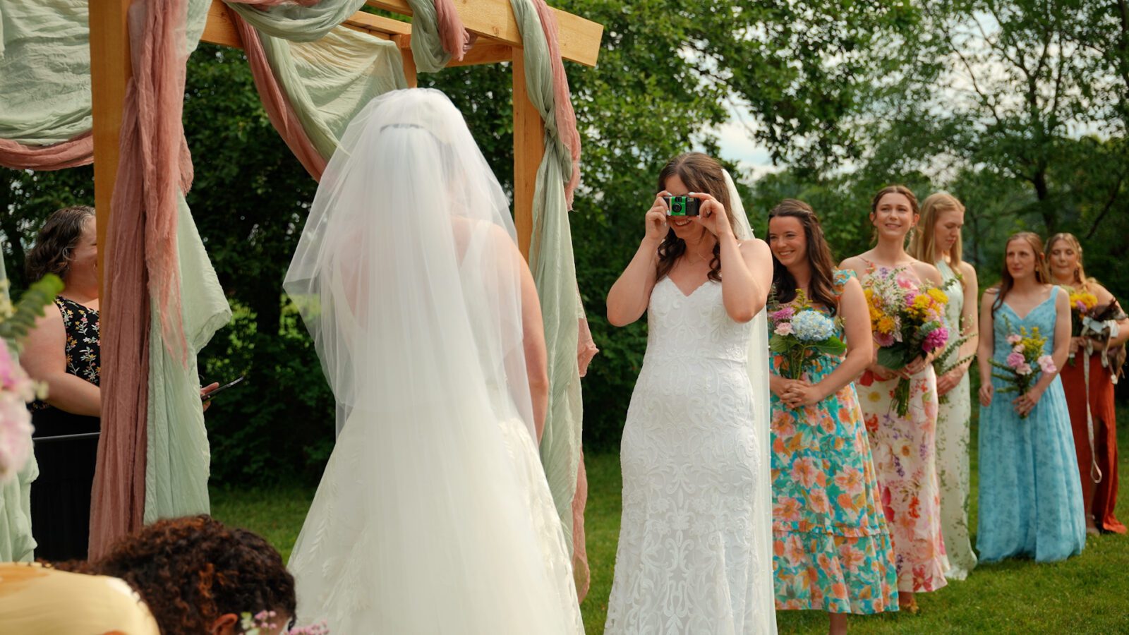 One newlywed taking a film photo of their partner during their outdoor wedding ceremony.