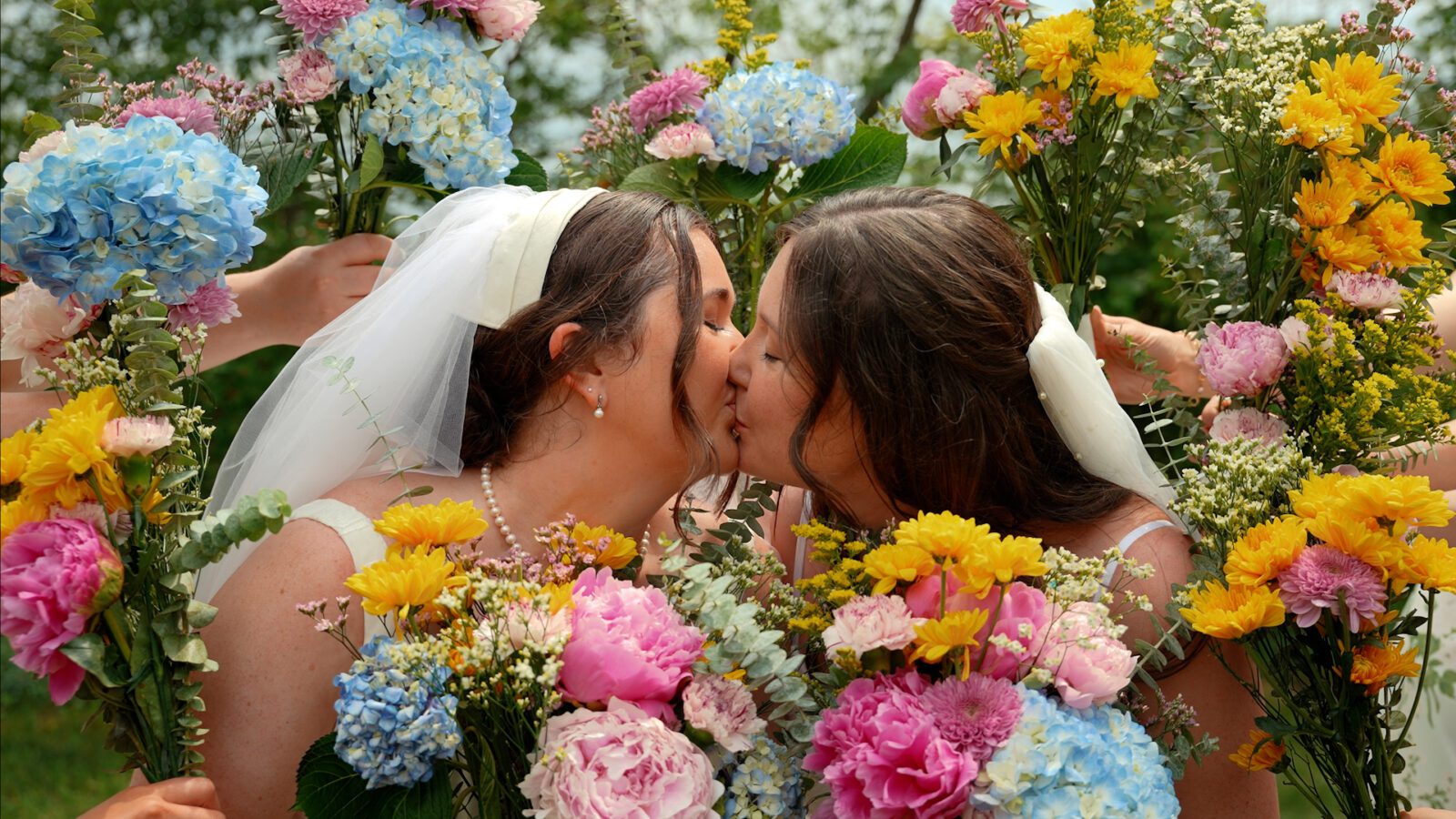 Newlyweds kissing surrounded by colorful wildflower bouquets at their District 5 Schoolhouse wedding.